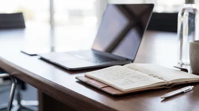 Creative workspace photograph with open notebook, handwritten notes, pen, and laptop on a warm wooden desk.
